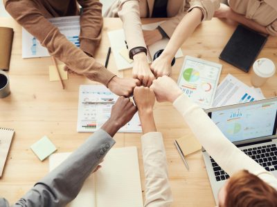 Top view of a diverse team fist bumping over a meeting table with paperwork and laptops, symbolizing teamwork.