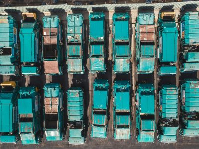 Aerial shot of turquoise garbage trucks parked in neat rows, showcasing a pattern of urban utility vehicles.
